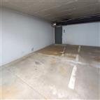 Prázdné parkovací stání v suterénu budovy se světlou omítnutou stěnou a betonovou podlahou, ideální pro bezpečné parkování